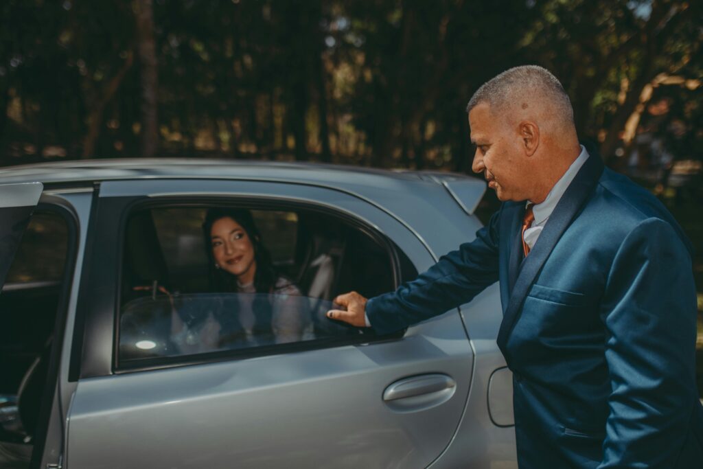 pexels-photo-18183694-18183694 A businessman in a suit opens a car door for a woman sitting inside under sunlight outdoors.