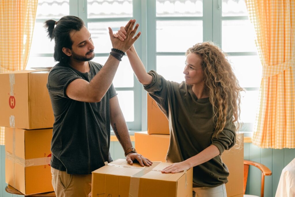 pexels-photo-4246202-4246202 Happy woman in casual wear standing near heap of cardboard boxes and giving high five to ethnic boyfriend with ponytail showing agreement while looking at each other