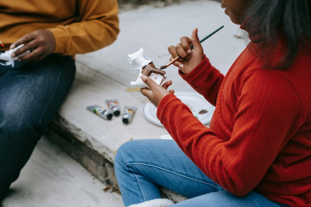 pexels-photo-5728200-5728200 Crop anonymous African American adolescents decorating figures with brush and paint while sitting on wooden stairs