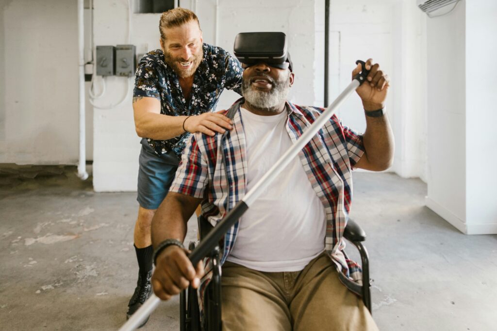 pexels-photo-8098279-8098279 Man assists wheelchair user engaged in rehabilitation exercise with VR set indoors.
